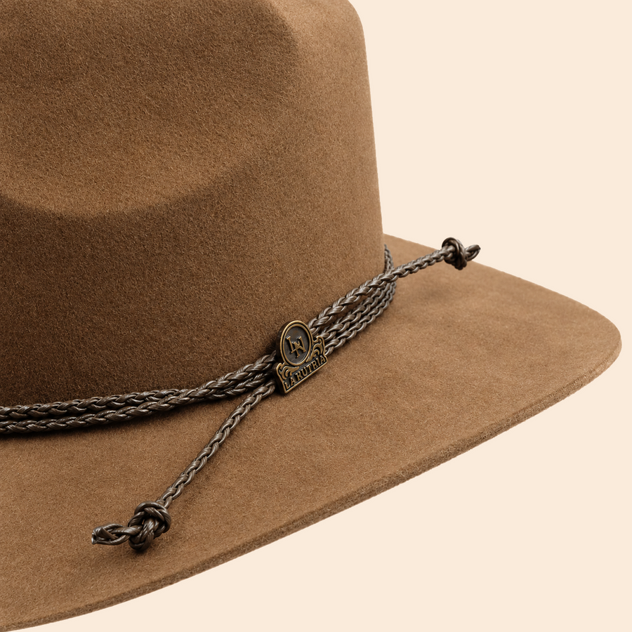 Detalle del sombrero marrón con cordón trenzado y distintivo metálico