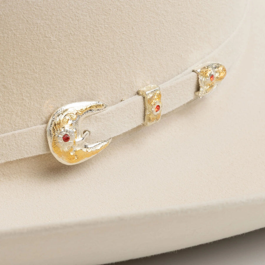 Detalle de la banda blanca del sombrero con hebilla y adornos metálicos dorados.