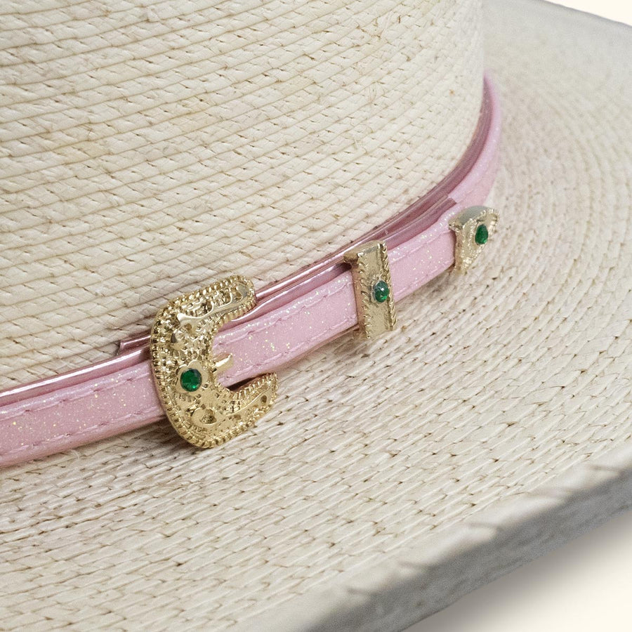 Detalle de cinta rosa y hebilla dorada con piedras verdes en sombrero de paja